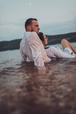 Günbatımında okyanusun dingin güzelliği arasında tutkulu bir öpücüğü paylaşan romantik genç bir çift.