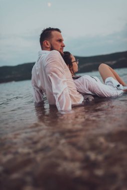 Günbatımında okyanusun dingin güzelliği arasında tutkulu bir öpücüğü paylaşan romantik genç bir çift.