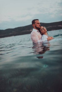 Sembolik ve duygusal olarak birbirine bağlı bir çift, sakin bir denizin arka planına nazikçe sarılır, nefes kesici bir gün batımının ılık renklerinde yıkanır.. 