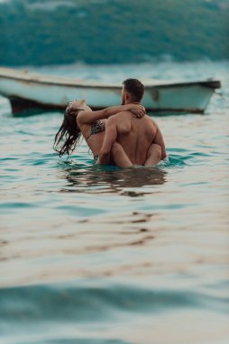 A romantic young couple sharing a passionate kiss amidst the serene beauty of the ocean at sunset clipart