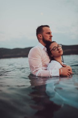 Sembolik ve duygusal olarak birbirine bağlı bir çift, sakin bir denizin arka planına nazikçe sarılır, nefes kesici bir gün batımının ılık renklerinde yıkanır.. 