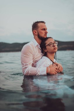 Sembolik ve duygusal olarak birbirine bağlı bir çift, sakin bir denizin arka planına nazikçe sarılır, nefes kesici bir gün batımının ılık renklerinde yıkanır.. 