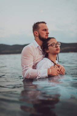 Sembolik ve duygusal olarak birbirine bağlı bir çift, sakin bir denizin arka planına nazikçe sarılır, nefes kesici bir gün batımının ılık renklerinde yıkanır.. 