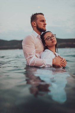 Sembolik ve duygusal olarak birbirine bağlı bir çift, sakin bir denizin arka planına nazikçe sarılır, nefes kesici bir gün batımının ılık renklerinde yıkanır.. 