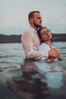 Sembolik ve duygusal olarak birbirine bağlı bir çift, sakin bir denizin arka planına nazikçe sarılır, nefes kesici bir gün batımının ılık renklerinde yıkanır.. 