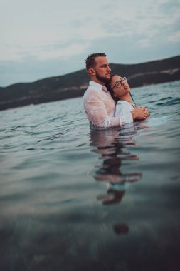 Sembolik ve duygusal olarak birbirine bağlı bir çift, sakin bir denizin arka planına nazikçe sarılır, nefes kesici bir gün batımının ılık renklerinde yıkanır.. 