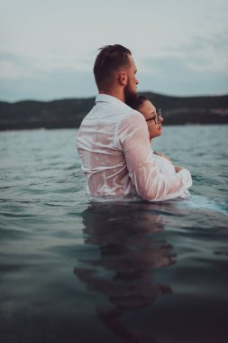 Sembolik ve duygusal olarak birbirine bağlı bir çift, sakin bir denizin arka planına nazikçe sarılır, nefes kesici bir gün batımının ılık renklerinde yıkanır.. 