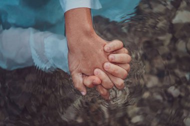Yakın çekimde romantik bir çiftin elleri su yüzeyinin altında birbirine dolanır, duyusal bir kucaklaşmayla aşklarının dokunsal ve suda yaşayan özünü yakalar.. 