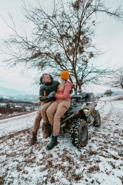  Romantik bir çift, karlı arazide neşeyle bir avluya binerken şefkatli bir kucaklaşmayı ve öpüşmeyi paylaşır. Kış macerasının ortasında büyülü ve tutkulu bir an yaratır.. 