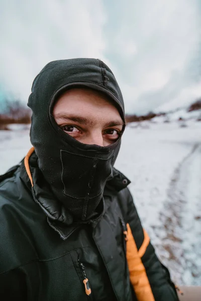 In this dynamically captured wide-angle photograph, a rugged man in a balaclava is seen up close, gearing up for an extreme quad ride through the snow, showcasing anticipation and readiness for an