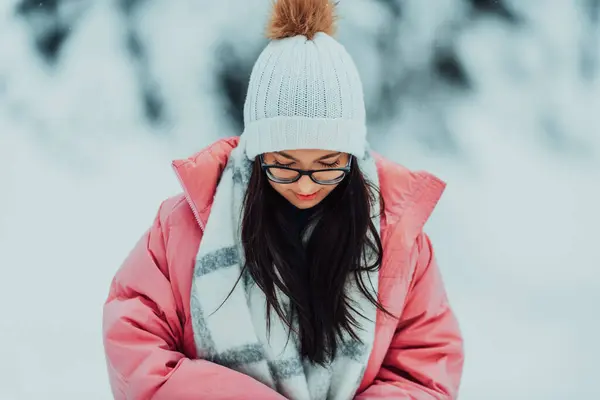 In a picturesque snowy landscape, a charming woman in a pink jacket and white hat exudes joy and style on a beautiful winter day.