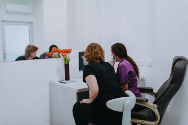 Modern bir diş muayenehanesinde, bir dişçi ve genç bir hasta yeni diş gözlüklerinin araştırılması ve bilgisayar kullanarak tedavi seçeneklerinin tartışılması gibi ortak bir konsültasyona girişirler.. 