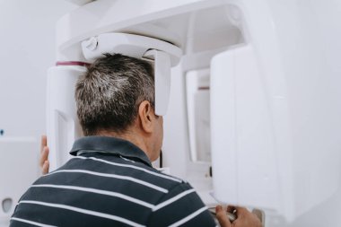 Modern bir diş kliniğinde ileri seviye teşhis ve tedavi planlaması için 3 boyutlu diş taraması yaptıran yaşlı bir adam.. 