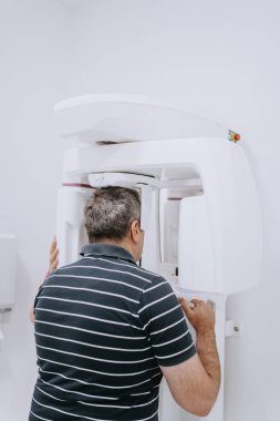 Modern bir diş kliniğinde ileri seviye teşhis ve tedavi planlaması için 3 boyutlu diş taraması yaptıran yaşlı bir adam.. 