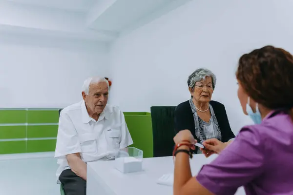 An elderly couple engages in a thoughtful discussion with their dentist about modern denture options in a contemporary dental office setting.