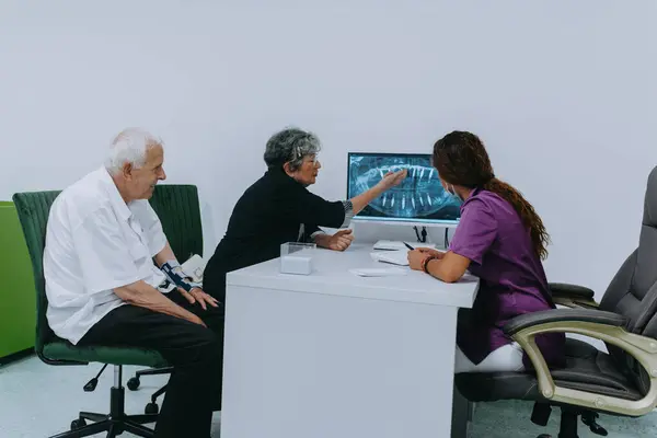 An elderly couple engages in a thoughtful discussion with their dentist about modern denture options in a contemporary dental office setting.