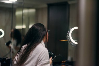 Kulağında kulaklıkla neşeli bir kadın, banyoda saç kurutma makinesiyle saçlarını kurular, kaygısız ve enerjik bir kişisel bakım ve rahatlama anını somutlaştırır.. 