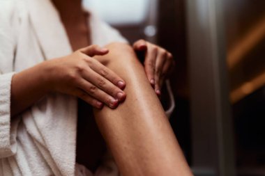 Bir kadın kendine bakım rutinine kendini kaptırır. Rahatlatıcı bir banyodan sonra bacaklarına krem sürerek cildini şımartır. Güzelliğin ve refahın özünü kucaklar.. 