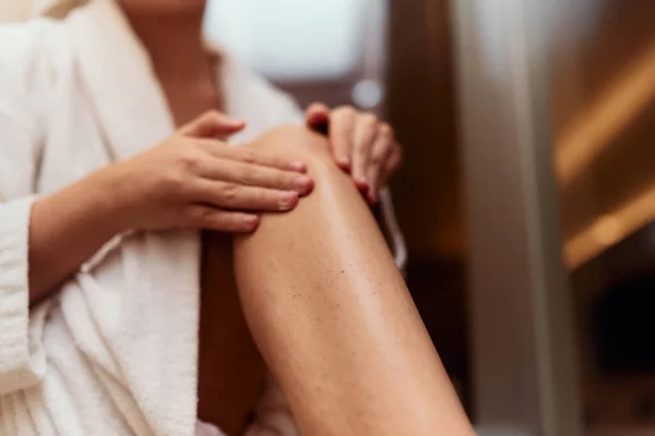 A woman indulges in her self care routine, pampering her skin after a relaxing bath by applying hydrating cream to her legs, embracing the essence of beauty and well being.