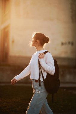 Güzel bir Avrupalı genç, yandan çekilmiş bir portreyle okuldan sonra gün batımında sırtında sırt çantasıyla eve yürür..