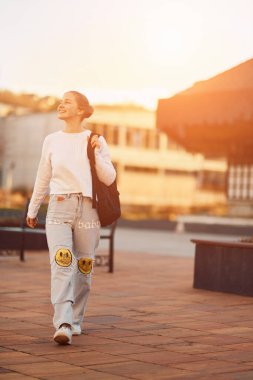 Güzel sarışın bir genç gün batımında okuldan eve döner, okul çantasını huzurlu ve huzurlu bir şehir ortamında taşır.. 