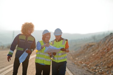 Mühendis ve işçilerden oluşan bir ekip, yenilenebilir enerjinin verimli bir şekilde üretilmesini sağlamak için birlikte çalışan modern bir rüzgâr çiftliğinde rüzgar türbini projesini denetliyor.. 