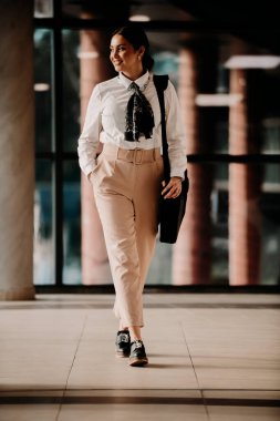 Zarif bir Latin iş kadını, çantasıyla modern ofisinde rahatça dolaşır ve kararlılığını belli eder.. 