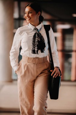 Zarif bir Latin iş kadını, çantasıyla modern ofisinde rahatça dolaşır ve kararlılığını belli eder.. 