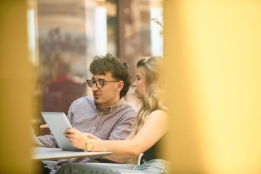 A dynamic business couple sits in a cafe, engrossed in paperwork, utilizing tablets, and engaging in thoughtful discussions as they strategize and plan their entrepreneurial ventures clipart