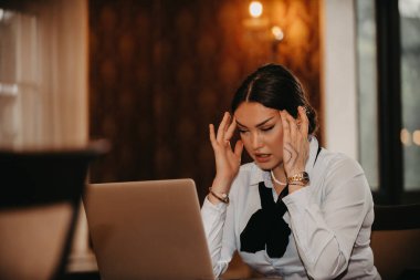 Yorgun bir Latin iş kadını laptopuna konsantre olmak için kahve içerken mesleki yolculuğunun zorluklarını ve kararlılığını yansıtıyor..