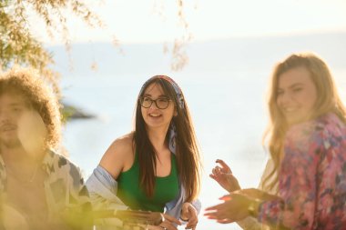 Bir grup arkadaş plajda toplanıp müzik, kahkaha ve birlikteliğin sıcaklığıyla dolu neşeli anları paylaşıyorlar. Gençler sahilde eğleniyor.