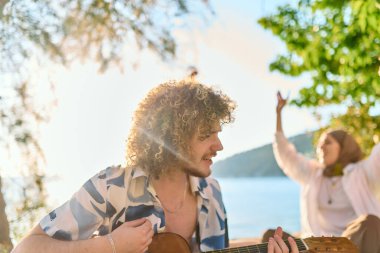 Bir grup arkadaş plajda toplanıp müzik, kahkaha ve birlikteliğin sıcaklığıyla dolu neşeli anları paylaşıyorlar. Gençler sahilde eğleniyor.