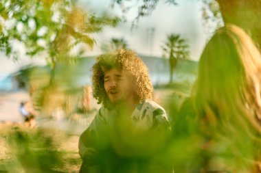 Bir grup arkadaş plajda toplanıp müzik, kahkaha ve birlikteliğin sıcaklığıyla dolu neşeli anları paylaşıyorlar. Gençler sahilde eğleniyor.