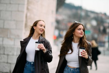 İki güzel iş kadını ellerinde kahve fincanlarıyla işe giderler..