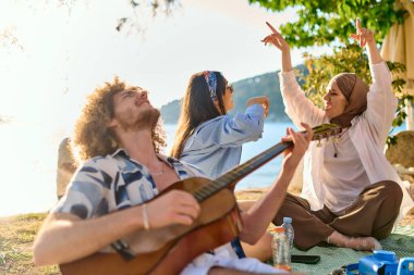 Bir grup arkadaş plajda toplanıp müzik, kahkaha ve birlikteliğin sıcaklığıyla dolu neşeli anları paylaşıyorlar. Gençler sahilde eğleniyor.