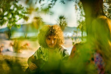 Bir grup arkadaş plajda toplanıp müzik, kahkaha ve birlikteliğin sıcaklığıyla dolu neşeli anları paylaşıyorlar. Gençler sahilde eğleniyor.