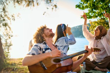 Bir grup arkadaş plajda toplanıp müzik, kahkaha ve birlikteliğin sıcaklığıyla dolu neşeli anları paylaşıyorlar. Gençler sahilde eğleniyor.