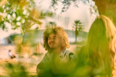 Bir grup arkadaş plajda toplanıp müzik, kahkaha ve birlikteliğin sıcaklığıyla dolu neşeli anları paylaşıyorlar. Gençler sahilde eğleniyor.
