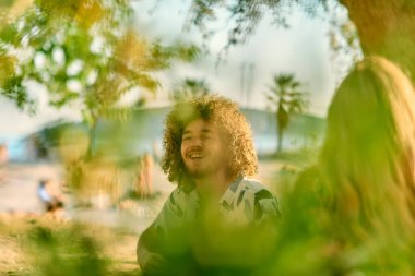 Bir grup arkadaş plajda toplanıp müzik, kahkaha ve birlikteliğin sıcaklığıyla dolu neşeli anları paylaşıyorlar. Gençler sahilde eğleniyor.