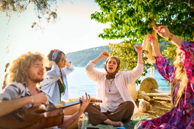 Bir grup arkadaş plajda toplanıp müzik, kahkaha ve birlikteliğin sıcaklığıyla dolu neşeli anları paylaşıyorlar. Gençler sahilde eğleniyor.