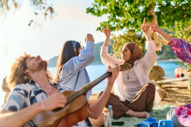 Bir grup arkadaş plajda toplanıp müzik, kahkaha ve birlikteliğin sıcaklığıyla dolu neşeli anları paylaşıyorlar. Gençler sahilde eğleniyor.