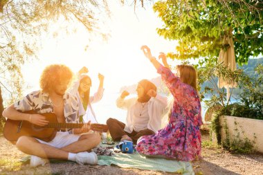 Bir grup arkadaş plajda toplanıp müzik, kahkaha ve birlikteliğin sıcaklığıyla dolu neşeli anları paylaşıyorlar. Gençler sahilde eğleniyor.