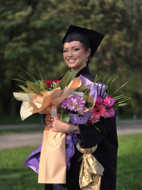 Güzel bir Latin mezunu elinde buketle mezuniyet töreninde diplomasını aldıktan sonra gururla gülümsüyor. 