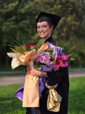 Güzel bir Latin mezunu elinde buketle mezuniyet töreninde diplomasını aldıktan sonra gururla gülümsüyor. 