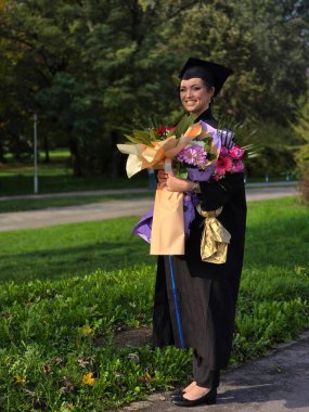 Güzel bir Latin mezunu elinde buketle mezuniyet töreninde diplomasını aldıktan sonra gururla gülümsüyor. 