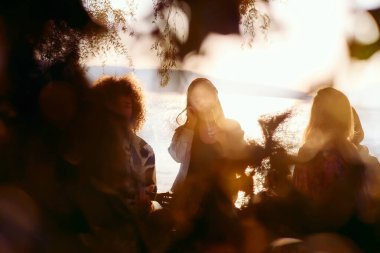 Bir grup arkadaş plajda toplanıp müzik, kahkaha ve birlikteliğin sıcaklığıyla dolu neşeli anları paylaşıyorlar. Gençler sahilde eğleniyor.