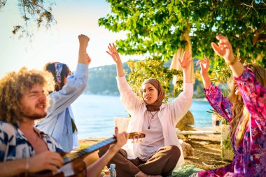 Bir grup arkadaş plajda toplanıp müzik, kahkaha ve birlikteliğin sıcaklığıyla dolu neşeli anları paylaşıyorlar. Gençler sahilde eğleniyor.