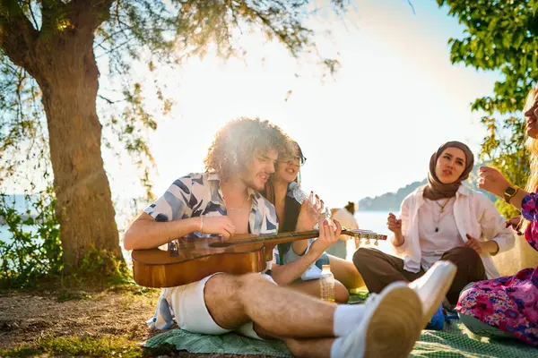 Bir grup arkadaş plajda toplanıp müzik, kahkaha ve birlikteliğin sıcaklığıyla dolu neşeli anları paylaşıyorlar. Gençler sahilde eğleniyor.