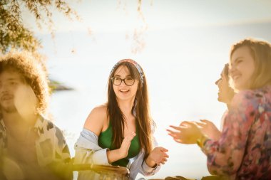 Bir grup arkadaş plajda toplanıp müzik, kahkaha ve birlikteliğin sıcaklığıyla dolu neşeli anları paylaşıyorlar. Gençler sahilde eğleniyor.