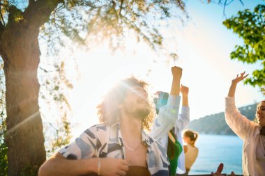 Bir grup arkadaş plajda toplanıp müzik, kahkaha ve birlikteliğin sıcaklığıyla dolu neşeli anları paylaşıyorlar. Gençler sahilde eğleniyor.